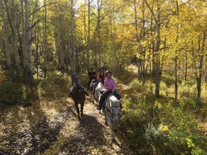 Family riding horses together along a scenic trail lined with golden aspen trees at Rusty Spurr Ranch in Colorado.