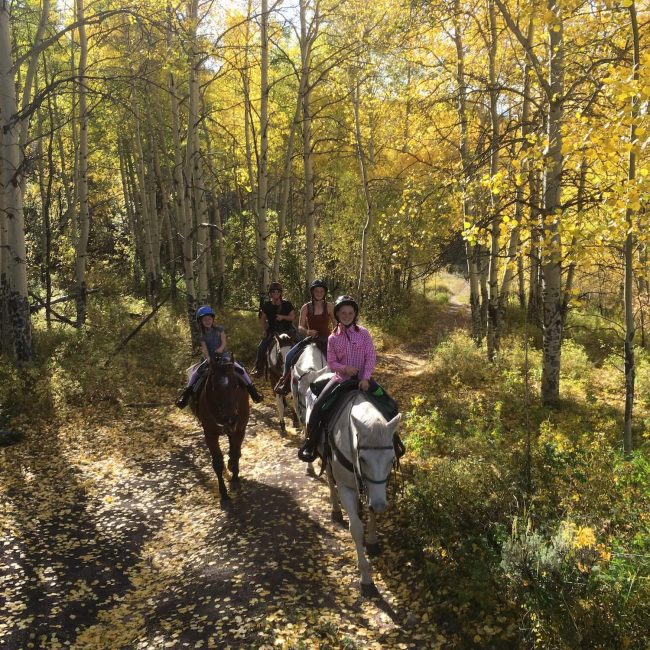 Family riding horses together along a scenic trail lined with golden aspen trees at Rusty Spurr Ranch in Colorado.