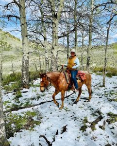 Rider leading a horse along a trail surrounded by golden aspen trees at Rusty Spurr Ranch in Colorado.