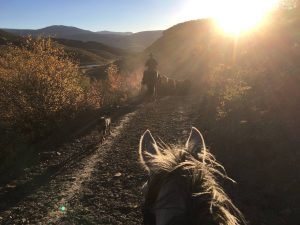 Stunning Colorado sunset over a western cattle ranch with riders and horses silhouetted at Rusty Spurr Ranch.