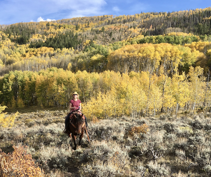 Scenic view of a horseback rider pausing to enjoy the stunning view of a colorful golden aspen valley at Rusty Spurr Ranch.