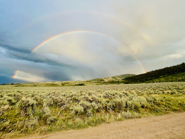 A colorful rainbow shines above the expansive landscape of the Rusty Spurr Ranch, highlighting the beautiful meadows.