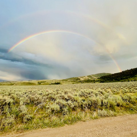 A colorful rainbow shines above the expansive landscape of the Rusty Spurr Ranch, highlighting the beautiful meadows.
